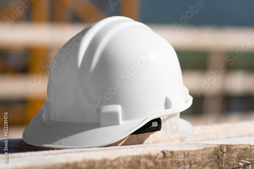 Close-up of a white helmet lying on a wooden beam on a construction site on a sunny day. Security concept