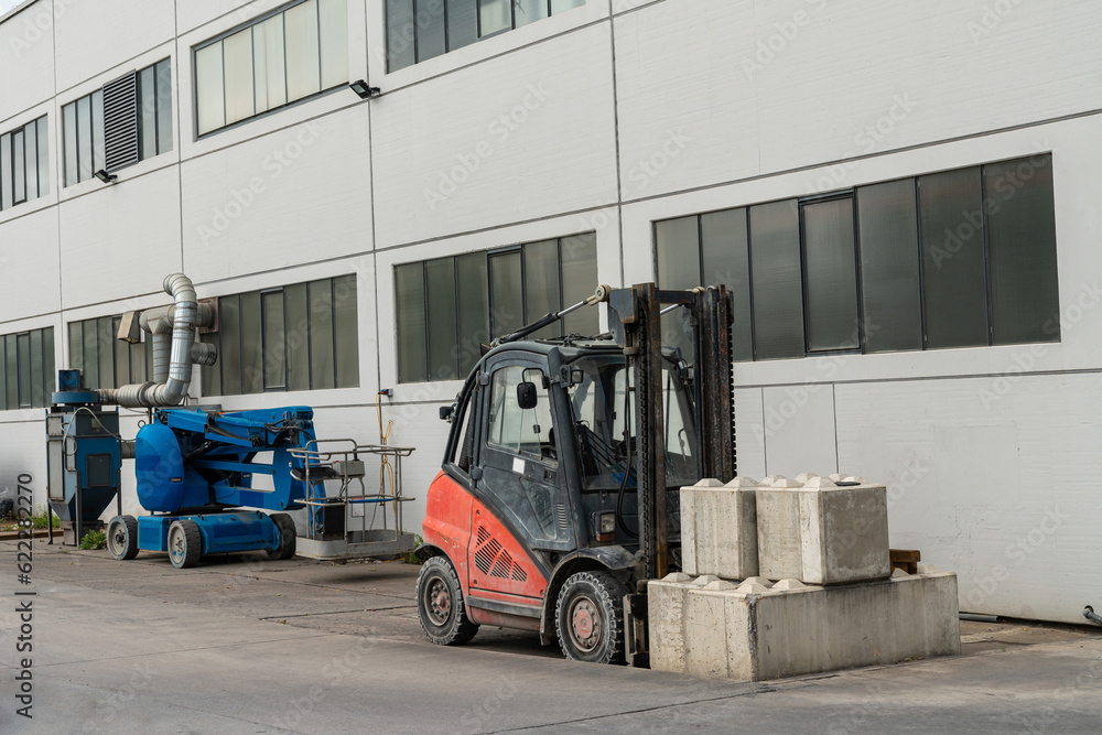 A small forklift with loaded concrete blocks stands near the building. Near the lift for people.