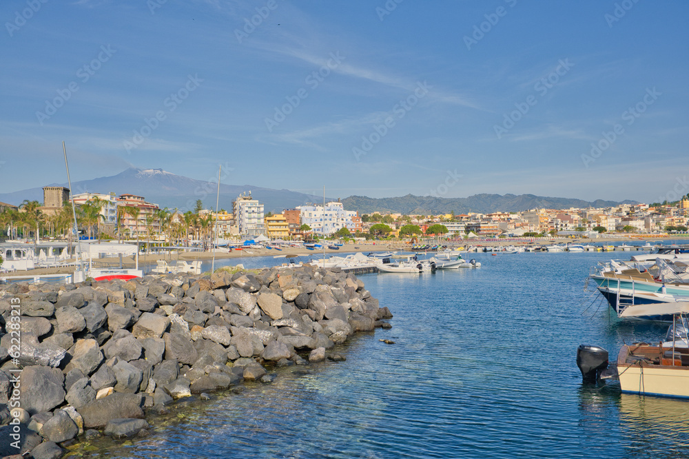 small boat harbor in Giardini Naxos overlooking Taormina high in the mountains, Sicily, Italy