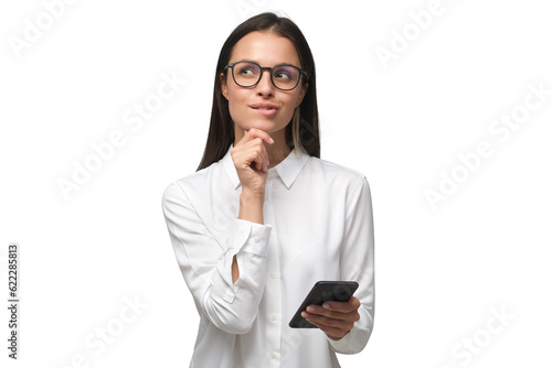 Young woman in white office shirt wearing eyeglasses and holding smartphone, making decisions and feeling doubt, looking away