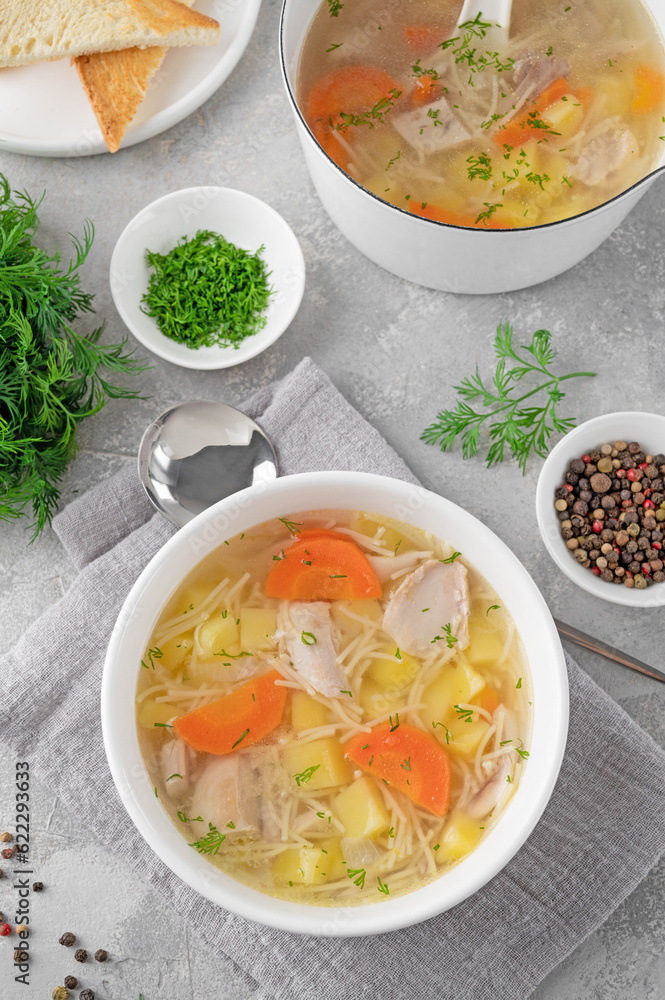 Chicken soup with noodles and vegetables in white bowl on a gray concrete background.