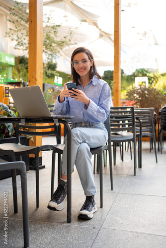 Freelancer using smartphone and laptop sitting outdoor cafe