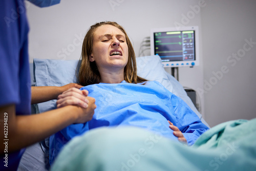 Pregnant woman, clinic and labor with push, holding hands or support in bed, baby and pain. Strong mother, childbirth process and helping hand in hospital bed for infant child, motivation or shouting
