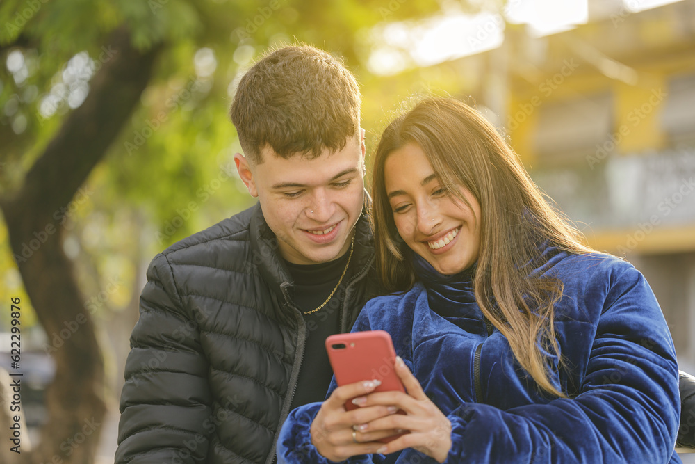 Medium shot of a girl and a boy sitting on the bench in a public park.