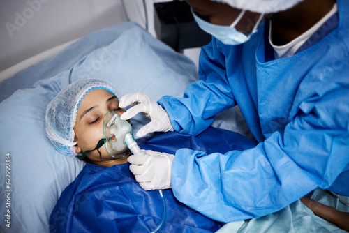 Doctor, hospital bed or woman with an oxygen mask, anesthesia or operation for healthcare recovery. Medical, ventilation or sick patient with breathing equipment in coma for respiratory in emergency photo