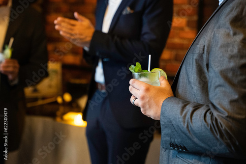 Close up of mojito cocktail in man hand in a business suit with blurred people in the background on the business event party. photo