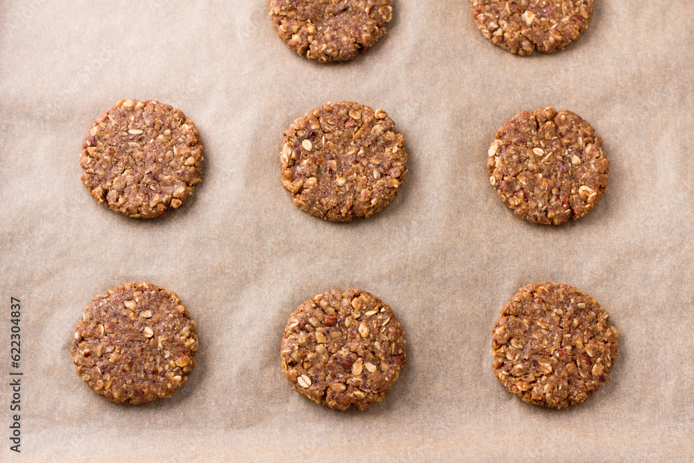 Fototapeta premium Raw halthy oatmeal cookies with dates, nuts and flaxseed on baking paper, top view. Cooking homemade vegan baking