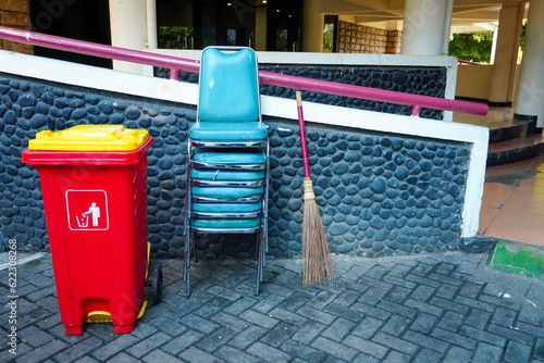Natural broom, red outdoor plastic waste bins, and stacked chairs in house yard photo