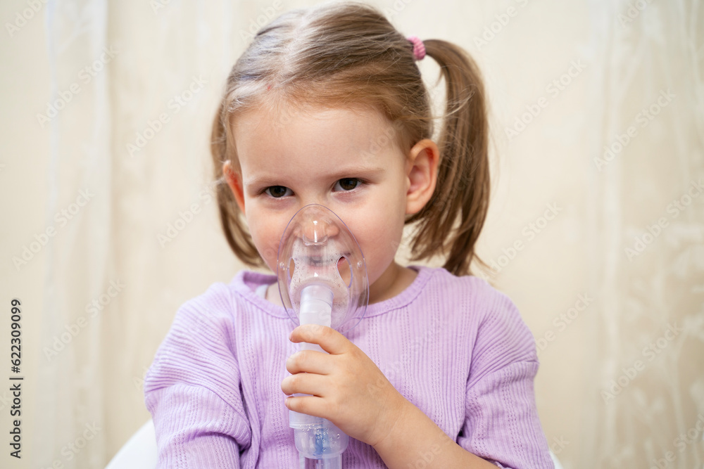 Cute little girl inhaling mist form nebulizer at home. Holding mask over her nose and mouth 
