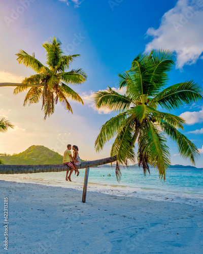Canvas-taulu Praslin Seychelles tropical island with white beaches and palm trees, a couple of men and woman watching sunset above a palm tree climbing in a palm tree at Anse Volber Seychelles