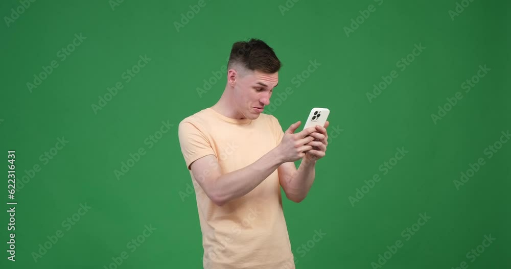 A Caucasian man appears surprised as he holds a phone against a vibrant green background. His eyes widen, and his mouth slightly agape, reflecting his astonishment. A Caucasian man appears surprised as he holds a phone against a vibrant green background. His eyes widen, and his mouth slightly agape, reflecting his astonishment.