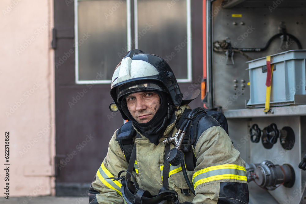 Portrait of a tired firefighter in a protective suit and a protective helmet sitting by a fire engine after returning to the fire department Portrait of a tired firefighter in a protective suit and a protective helmet sitting by a fire engine after returning to the fire department