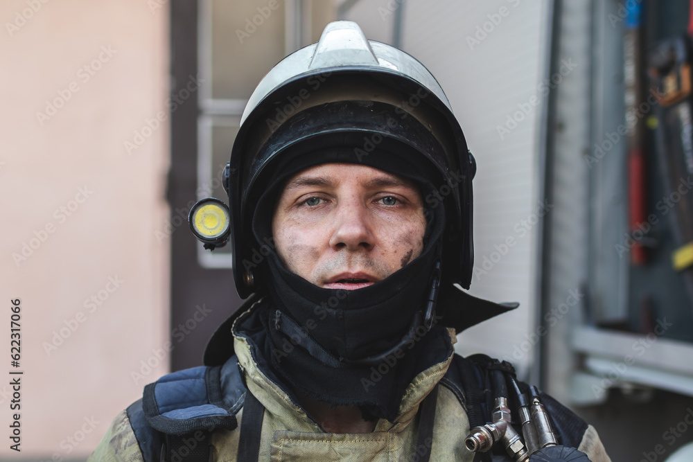 Portrait of a firefighter in a protective suit and a protective helmet standing by a fire engine after working on a fire. Close-up image Portrait of a firefighter in a protective suit and a protective helmet standing by a fire engine after working on a fire. Close-up image