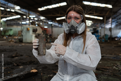 emergency pollution factory concept. Female chemist wearing PPE and gas mask inspecting oil on factory floor