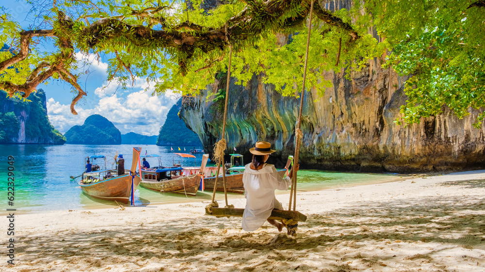 Naklejka premium women on a swing at the Tropical lagoon of Koh Loa Lading Krabi Thailand part of the Koh Hong Islands in Thailand. beautiful beach with limestone cliffs and longtail boats