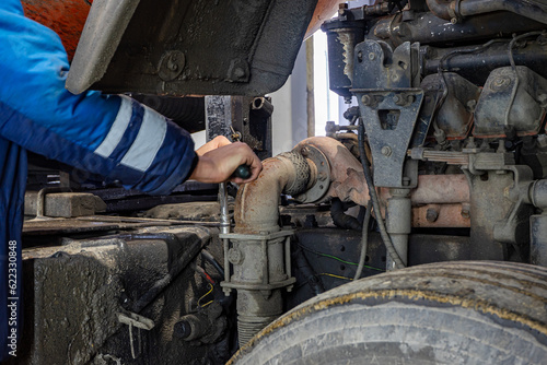 Car mechanic repairs large truck or tractor in workshop. Professional mechanic repairs truck engine.