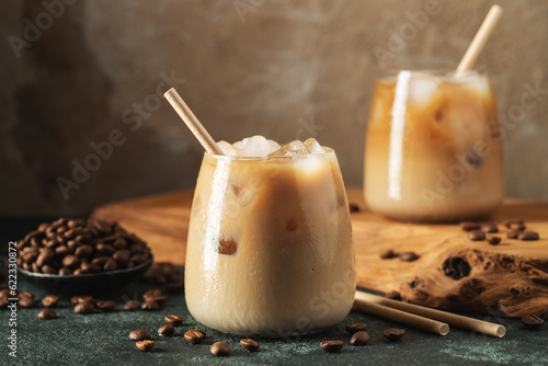Obraz na płótnie Ice coffee in a tall glass with cream poured over, ice cubes and beans on a dark concrete table