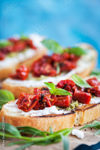 Bruschetta with cream cheese, pesto, fresh basil and sun dried tomatoes on blue rustic wooden table