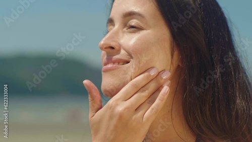 Close-up woman on bikini takes sunscreen of tube, moisturizing lotion applies sunblock on her face
