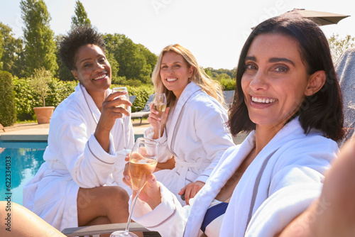POV Shot Of Mature Female Friends Wearing Robes Outdoors On Loungers Drinking Champagne On Spa Day
