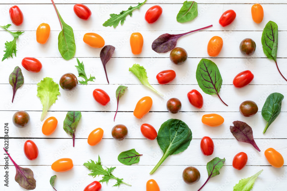 Various fresh green salad leaves and colorful cherry tomatoes on white wooden background. Flat lay. Top view