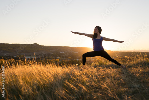 Woman doing yoga warrior II pose during evening sunset