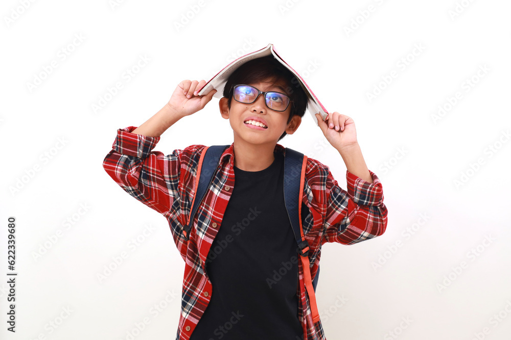 Happy asian student standing while putting a book on his head and looking above Happy asian student standing while putting a book on his head and looking above