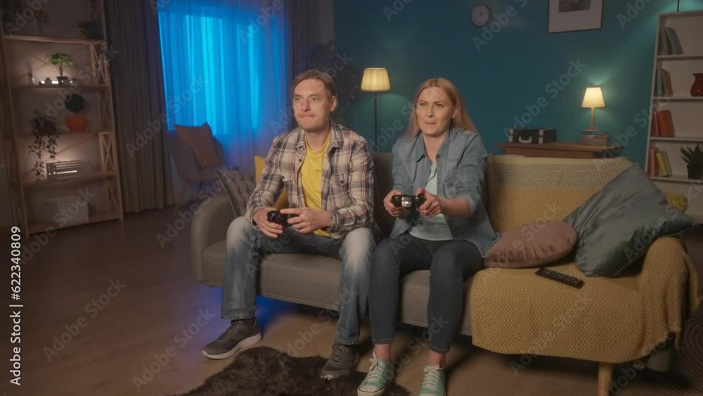 A woman and a man are playing a consular game with a game controller. The woman joyfully wins, points to herself, I am the BEST. The man is upset. Weekend leisure concept. HDR BT2020 HLG Material. A woman and a man are playing a consular game with a game controller. The woman joyfully wins, points to herself, I am the BEST. The man is upset. Weekend leisure concept. HDR BT2020 HLG Material.