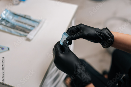 Close-up cropped top view of unrecognizable dentist in protective gloves opening package with new nozzle for polishing and grinding teeth of patient. Concept of teeth whitening  dental treatment.