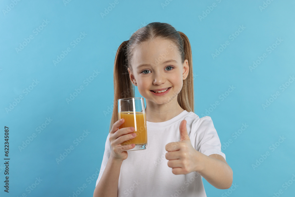 Cute little girl with fresh juice showing thumbs up on light blue background Cute little girl with fresh juice showing thumbs up on light blue background