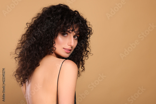 Beautiful young woman with long curly hair on beige background. Space for text