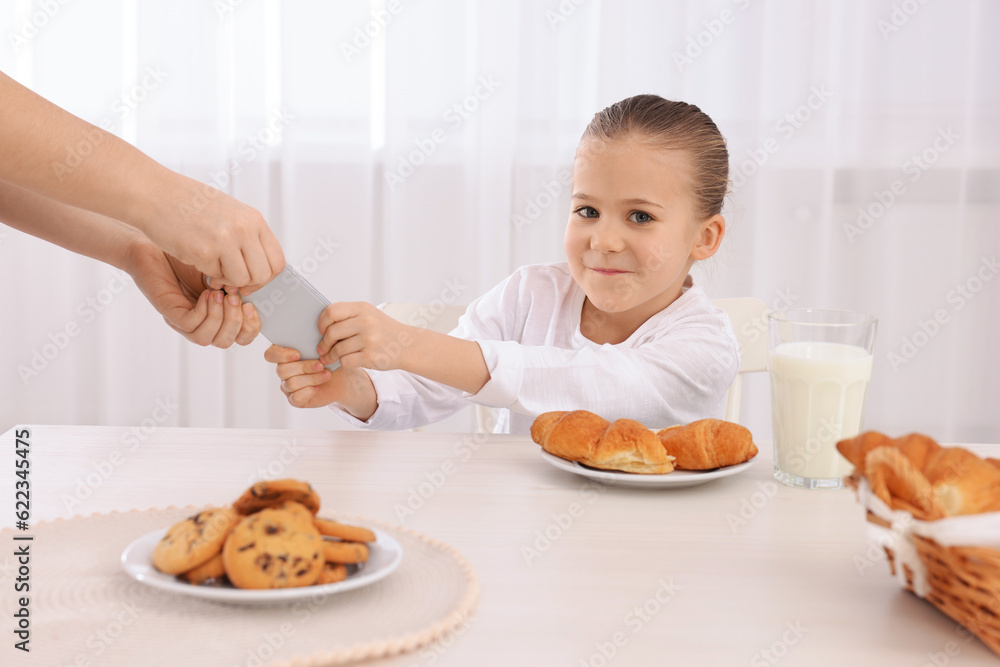 Woman taking away smartphone from her daughter at table indoors, closeup. Internet addiction Woman taking away smartphone from her daughter at table indoors, closeup. Internet addiction