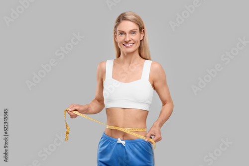 Slim woman measuring waist with tape on grey background. Weight loss © New Africa