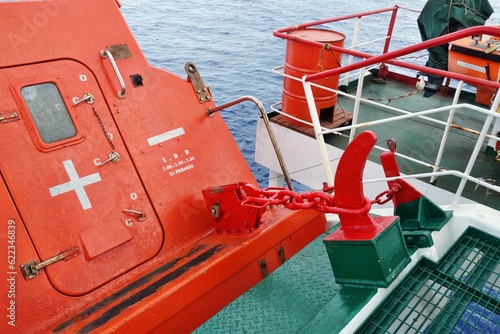 Photos View on release mechanism of orange free fall lifeboat with hook and chain secured on launching ramp on stern part of vessel and ready for abandon ship with crew during emergency situation