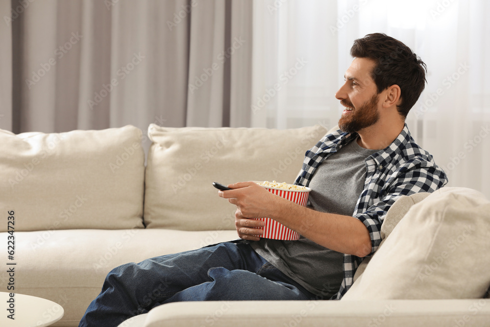Happy man watching TV with popcorn on sofa indoors Happy man watching TV with popcorn on sofa indoors