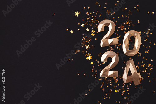 2024 gold colored numbers and glowing stars confetti on a black background. New Year concept with place for text.