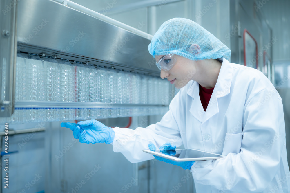 Female quality control worker inspecting water bottle on production line in drinking water factory Female quality control worker inspecting water bottle on production line in drinking water factory
