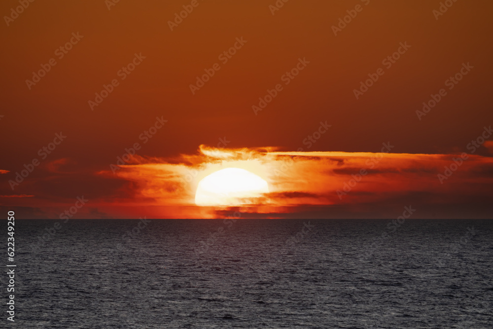 Naklejka premium Photo of a seascape, sunset, the sun goes beyond the horizon, close-up photo.