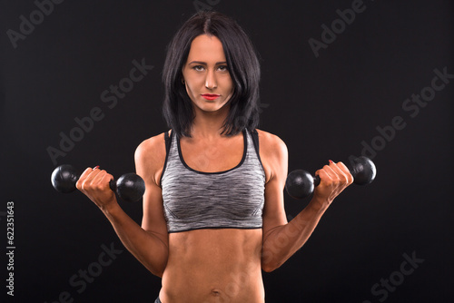 Sports and bodybuilding concepts. Fitness woman posing with dumbbells in both hands while posing for photographer isolated on black in studio. © Designpics