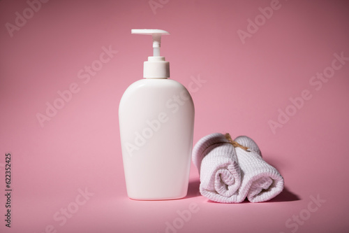 Shower gel, moisturizing lotion or body milk in white mockup bottle with dispenser and towel on pink isolated background