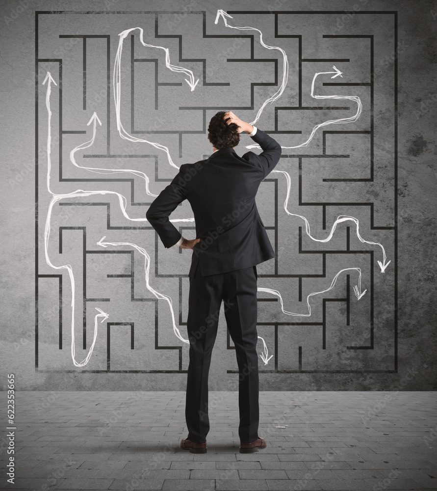 Confused business man seeks a solution to the labyrinth drawn on the wall Confused business man seeks a solution to the labyrinth drawn on the wall