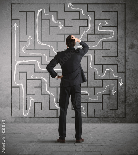 Foto Confused business man seeks a solution to the labyrinth drawn on the wall