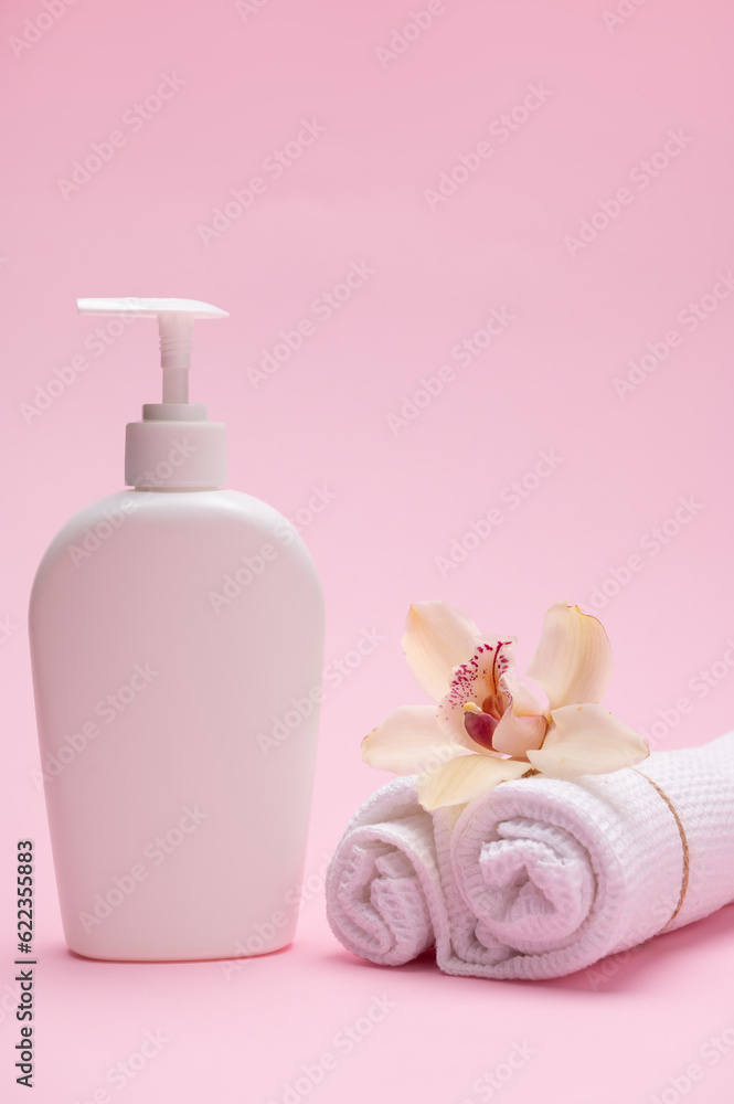 Vertical studio shot of a white mockup bottle with cosmetic product and orchid flower on rolled tied white waffle towels Vertical studio shot of a white mockup bottle with cosmetic product and orchid flower on rolled tied white waffle towels