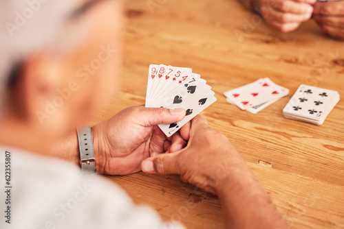Hands, cards and a senior man playing poker at a table in the living room of a retirement home. Gambling, planning and fun with an elderly male pensioner in a house closeup for entertainment games