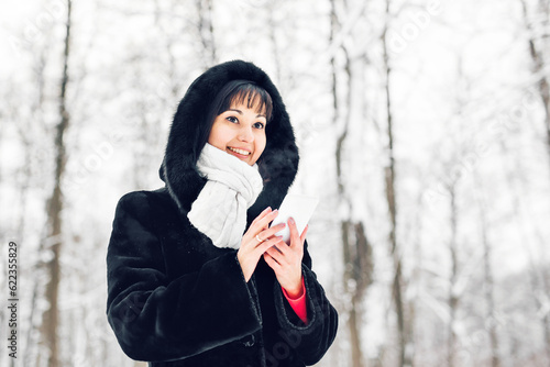 Young woman smiling with smart phone and winter landscape and snowflakes on the background.