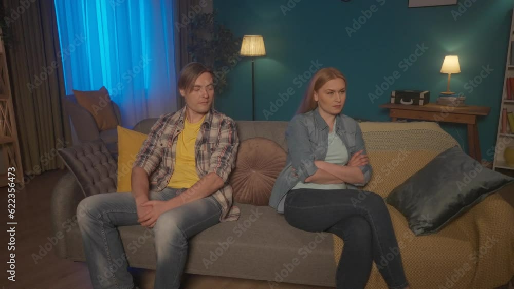 A married couple sits on the couch, turning their backs to each other. A man and a woman are offended, ignore each other after a conflict, quarrel. Problems in relationships. HDR BT2020 HLG Material. A married couple sits on the couch, turning their backs to each other. A man and a woman are offended, ignore each other after a conflict, quarrel. Problems in relationships. HDR BT2020 HLG Material.