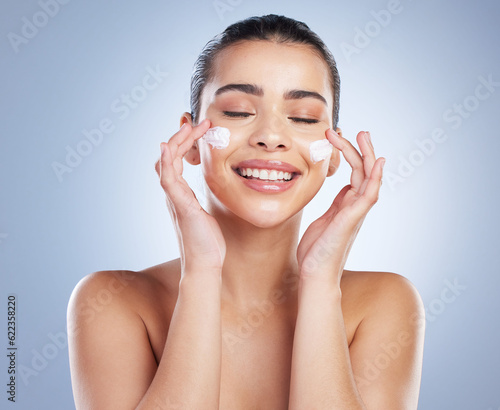 Skincare, hand and happy woman with face cream in studio for anti aging, wellness or hydration on grey background. Facial, smile and latino model with sunscreen, lotion or beauty mask application