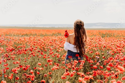 Woman poppies field. Back view of a happy woman with long hair in a poppy field and enjoying the beauty of nature in a warm summer day.