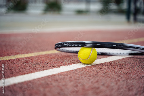 Closeup view on tennis ball and racket racquet lying on acrylic tennis hard court surface with empty blank copy space.