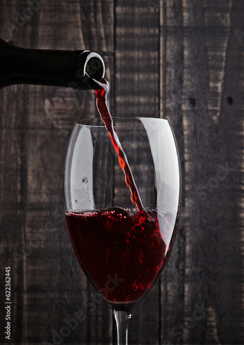 Pouring red wine into the glass from bottle on old wooden background